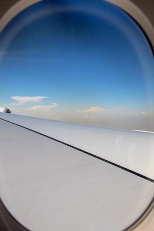 See through window on airplane with blue sky and clouds with wing