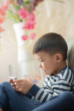 Asian child (boy) at home during lockdown, playing with smartphoneの写真素材