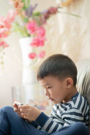 Asian child (boy) at home during lockdown, playing with smartphoneの写真素材