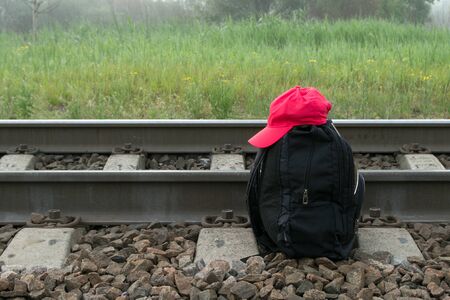 Black backpack with red cap on it next to railway in the background of meadow, greenary and fogの写真素材