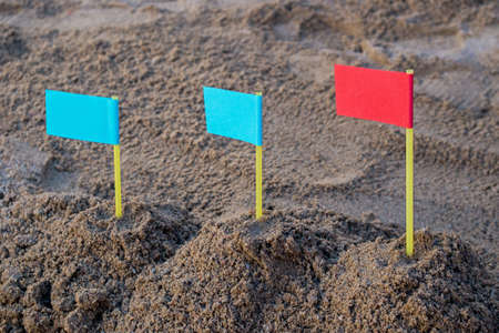 In children's sandbox three small hills of sand rising in height from left to right with two blue flags on the left and a red flag on the right. Concept: Right business strategy leads to leadershipの写真素材