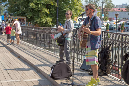 Street band of two guys with drum and guitar gives a concert on the Honey bridge across the river Pregolya, black bag in front of them, the railing - behind. KALININGRAD, RUSSIA â 1 SEPTEMBER, 2019のeditorial素材
