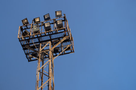 Old spotlight on a rectangular worn metal frame mounted on a shabby vertical support structure consisting of eight lamp elements used over the railway tracks on background of blue skyの写真素材