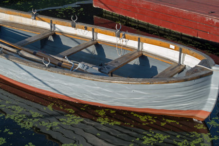Wooden boat located nose to the viewer at the red pier has gray sides with row of rowlocks, number...