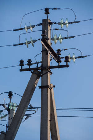 A gray concrete pillar with strung electric wires against a blue sky.の写真素材