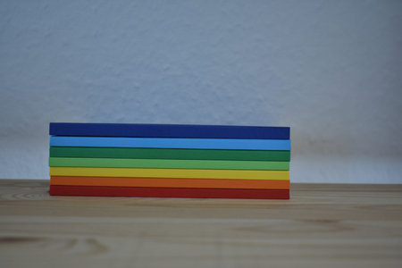 Rainbow colored books stacked on a wooden shelf European