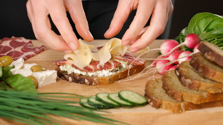 Woman's hands making sandwich with feta cheese and ham on wooden board, close-up