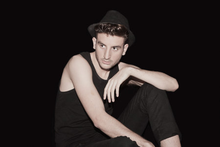 young boy dressed in black, with hat, black background