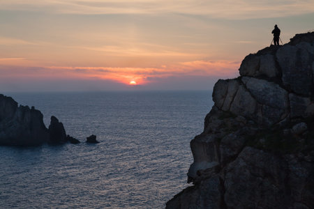 Man photographing the sunset on the rocks at a beachの写真素材