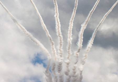 Smoke streaks fanning out from airplanes with a cloudy blue sky