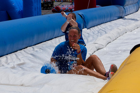 Friends sliding "happy endings" waterslide obstacle at the finish of the Wipeout 5K Run obstacles course in Wilmington Delaware  The Wipeout Run is themed after the popular ABC game show "Wipeout" and has12 obstacles. Some of the obstacles incorporated inのeditorial素材