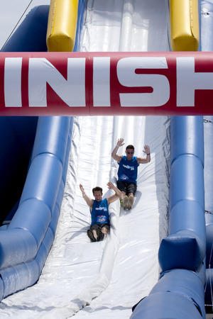 Friends sliding "happy endings" waterslide obstacle at the finish of the Wipeout 5K Run obstacles course in Wilmington Delaware  The Wipeout Run is themed after the popular ABC game show "Wipeout" and has12 obstacles. Some of the obstacles incorporated inのeditorial素材
