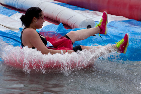 Woman splashes into the bottom of the "tumble tubes" water slide obstacle at the Wipeout 5K Run obstacles course in Wilmington Delaware  The Wipeout Run is themed after the popular ABC game show "Wipeout" and has12 obstacles. Some of the obstacles incorpoのeditorial素材