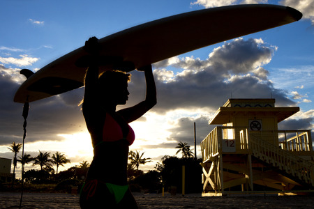 Silhouette of woman with surfboard on a beachの写真素材