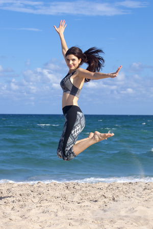Pretty woman jumping with excitement on a beach with ocean in the backgroundの写真素材