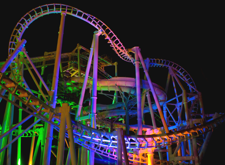 Modern rollercoaster lit up with different colors of light at night.の写真素材