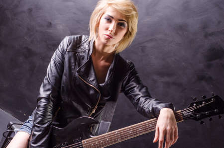 Beautiful young blonde dressed in black leather jacket with electric guitar on a black backgroundの写真素材