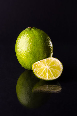 One whole lime with cuted slice on black background, vertical shot