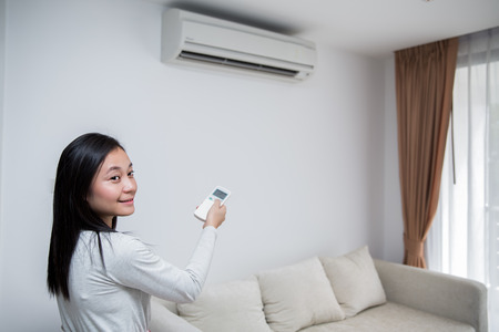 Beautiful girl holding a remote control air conditionerの写真素材
