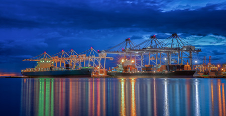 Container Cargo freight ship with working crane bridge in shipyard at dusk for Logistic Import Export backgroundの写真素材