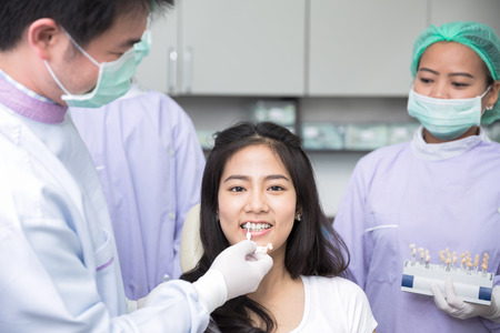 Dentist comparing patient's teeth shade with samples for bleaching treatmentの写真素材