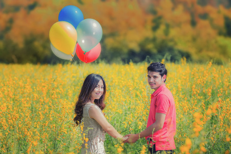 Valentines day concept, Young couple in love, Attractive man and woman enjoying romantic date at the Autumn garden with Balloon and yellow flowerの写真素材