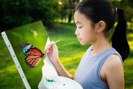 little painter at work in the butterfly with palette and canvas, butter fly drawing with gild in park wint green outdoor backgroung, kid, teen and student concept.の写真素材
