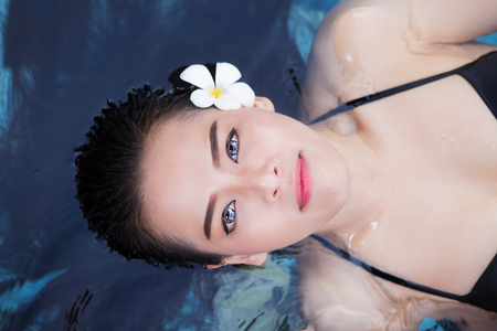 Attractive young asia woman floating in a swimming pool  looking at the sky with blue water. resort, hotel, spa and relax conceptの写真素材