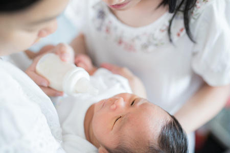 Sister and Mother takecare asian new born baby to feed and sleep in thr cradleの写真素材