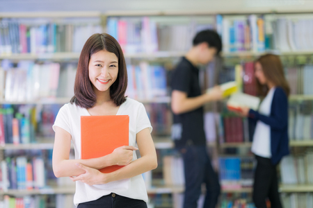 Asian student lady smile and read a book in library in university with her friends, education, student, library and university conceptの写真素材