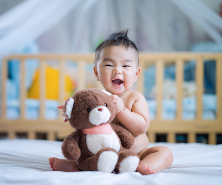 Asian new born baby sit and hug a teddy bear on ther bed in bed room, children, kid, toy, mom, family and house comceptの写真素材