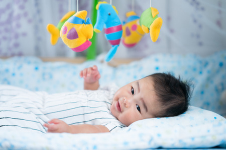 Asian newborn baby smile in a bed with fish and animal mobile. for mom, mother, family conceptの写真素材