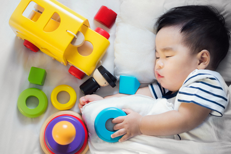 Asian baby sleep with wooded toy after playing on a bed in bedroomの写真素材