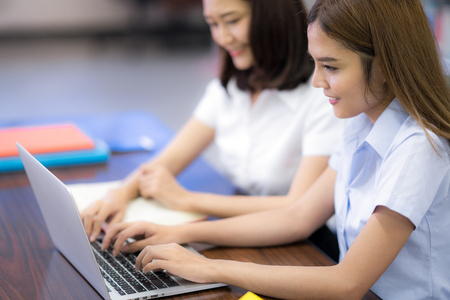 Asian student in Thai university mske a homework in library by computer note book and wifi internet togather in her universityの写真素材