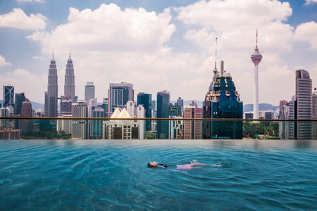 Asian girl swimming in roof top swimming pool in hotel in Kuala Lumpur city with landmark building and tower background, Kuala Lumpur, Malaysiaのeditorial素材