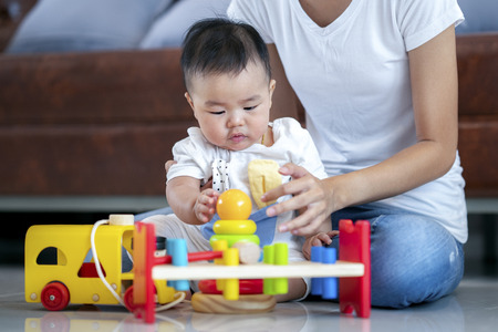 Mother play with her baby by wooded toy in living room, this image can use for family, insurance and mon conceptの写真素材