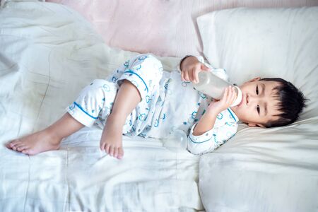 Asian boy drink a milk from bottle and sleep on bed roomの写真素材