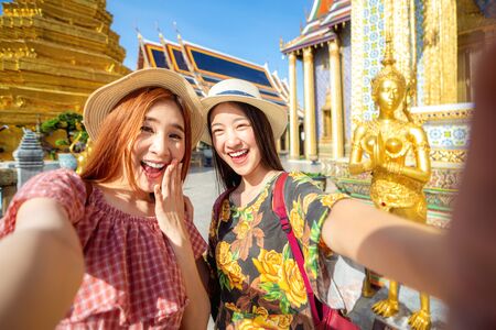 Two asian girlfriends traveling and selfie by camera in smartphone in Grand Palace and Wat phra kaew Bangkok cityの写真素材