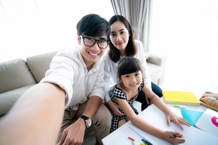 Asian family do homework and take selfie by smartphone togather in living room, this photo can use for family, education, study and home conceptの写真素材