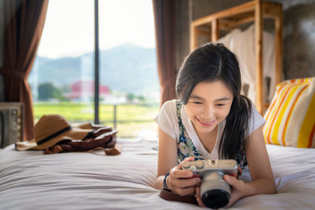 Thai girl relax in bed room with country background and check her photo from her camera in her home...