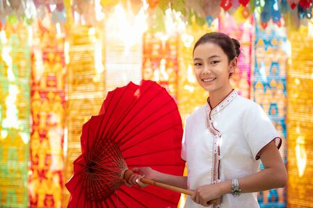 Asian girl in northern traditional costume and red umbrella stand in temple, this image can use for Chiang mai, Chiang rai and Nan conceptの写真素材