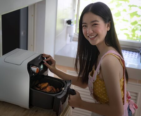 Asian girl cooking a fried chicken by Air Fryer machine in her kitchen at homeの写真素材
