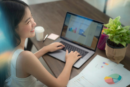 Asian girl typing data to her computer notebook for prepare her report on the wooden deak with the...