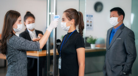 woman officer use scaner thermometer check a temperature of all person before pass to office inside...