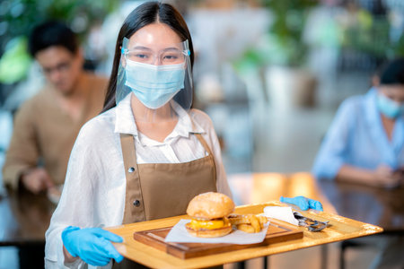 Beautiful young waitress with face protective mask working in exclusive restaurant. Coronavirus or Covid-19 concept.の写真素材