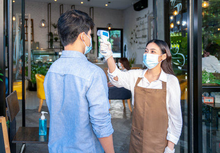 restaurant staff checking scan fever by digital thermometer to customer for protect infection coronavirus (covid-19) before enter cafe restaurant, social distancing, healthcare and medical conceptの写真素材