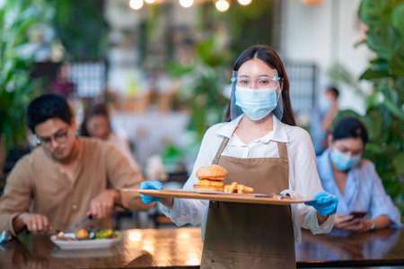 Beautiful young waitress with face protective mask working in exclusive restaurant. Coronavirus or Covid-19 concept.の写真素材