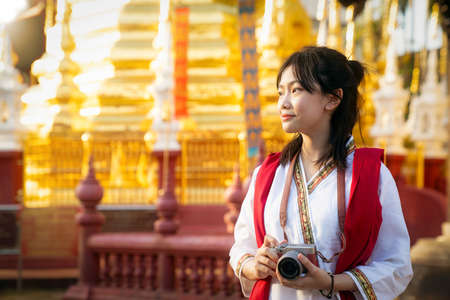 Asian traveller with camera on hand and vintage costume walking in Chiang mai city with golden pogoda and temple background, Thailandの写真素材