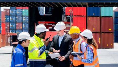 Manager standing and meeting with his staff in container depo company area. Worker in logistic and import export hub business standing and smileの写真素材
