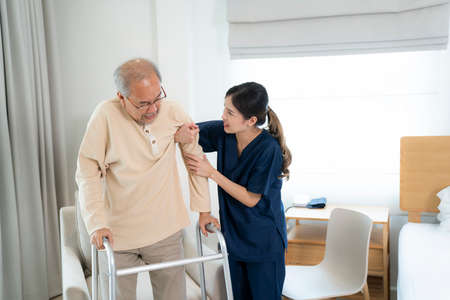 Asian nurse in nursing home support old man for standing and walking with staff,の写真素材